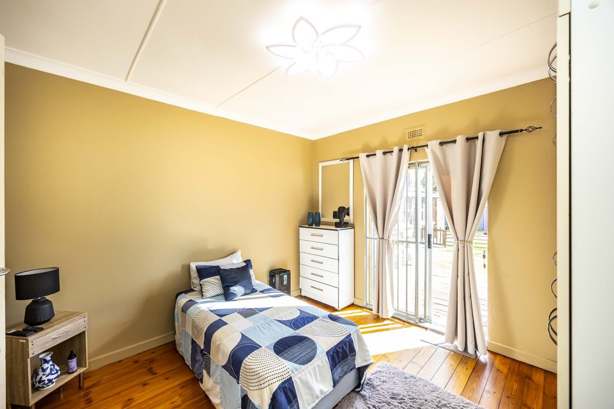 A bedroom featuring polished hardwood flooring, neutral wall tones, and a sliding glass door providing direct access to the outdoor area.