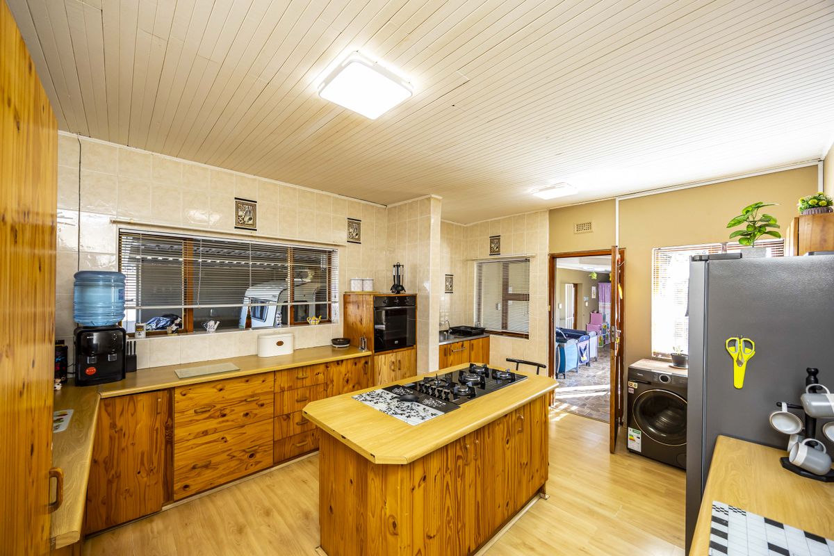 A functional kitchen featuring timber cabinetry, a central island with a gas hob, built-in oven, and tiled splashbacks, offering a traditional aesthetic.