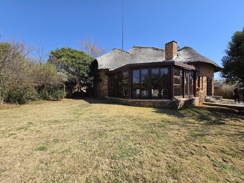 Rear view of a traditional thatch-roof house featuring a brick facade, an enclosed sunroom, and a spacious garden area.