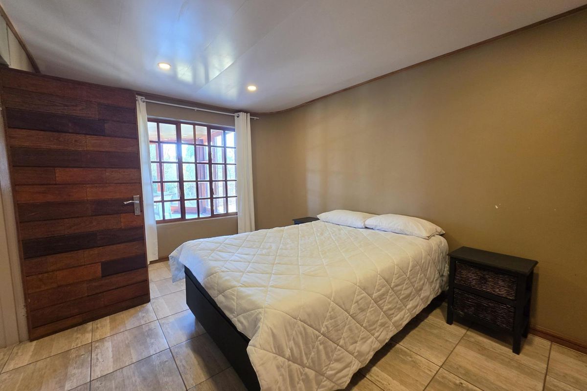 A bedroom featuring tiled flooring, recessed ceiling lights, and a timber-paneled feature wall with a timber-framed window.