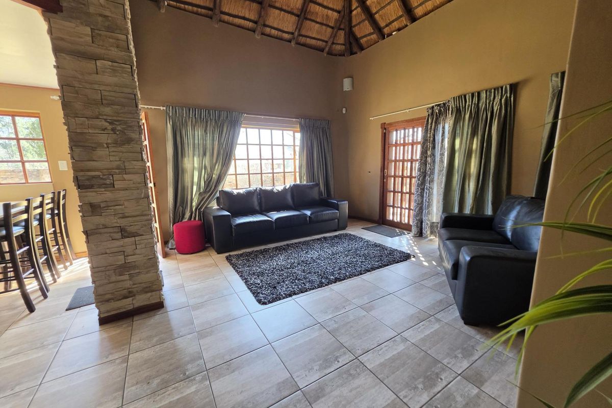 Spacious living room featuring a high thatched ceiling, stone-clad feature pillar, tiled flooring, and large timber-framed windows providing natural light.