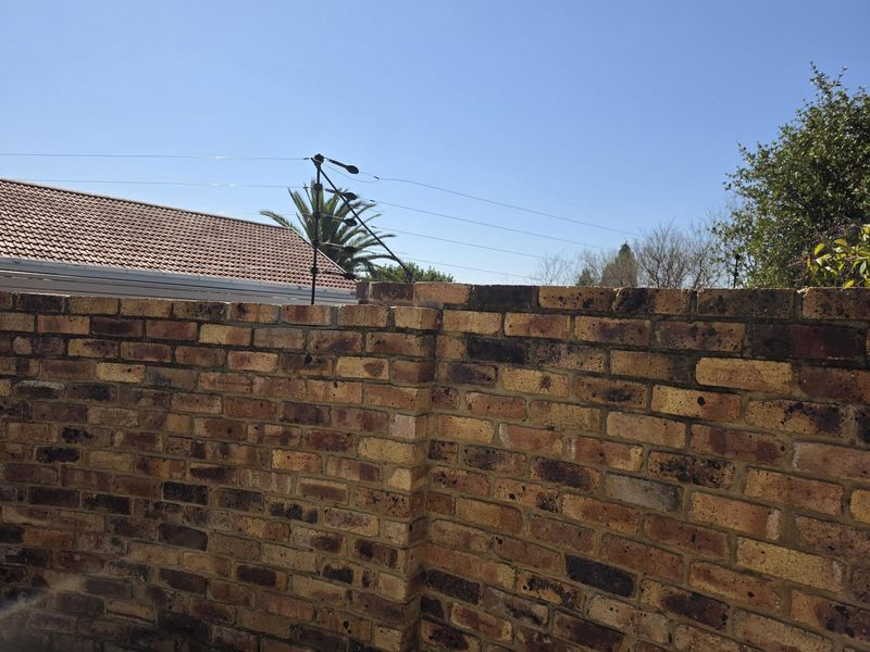 A view of a brick boundary wall featuring installed electric fencing, showing standard exterior maintenance and construction.