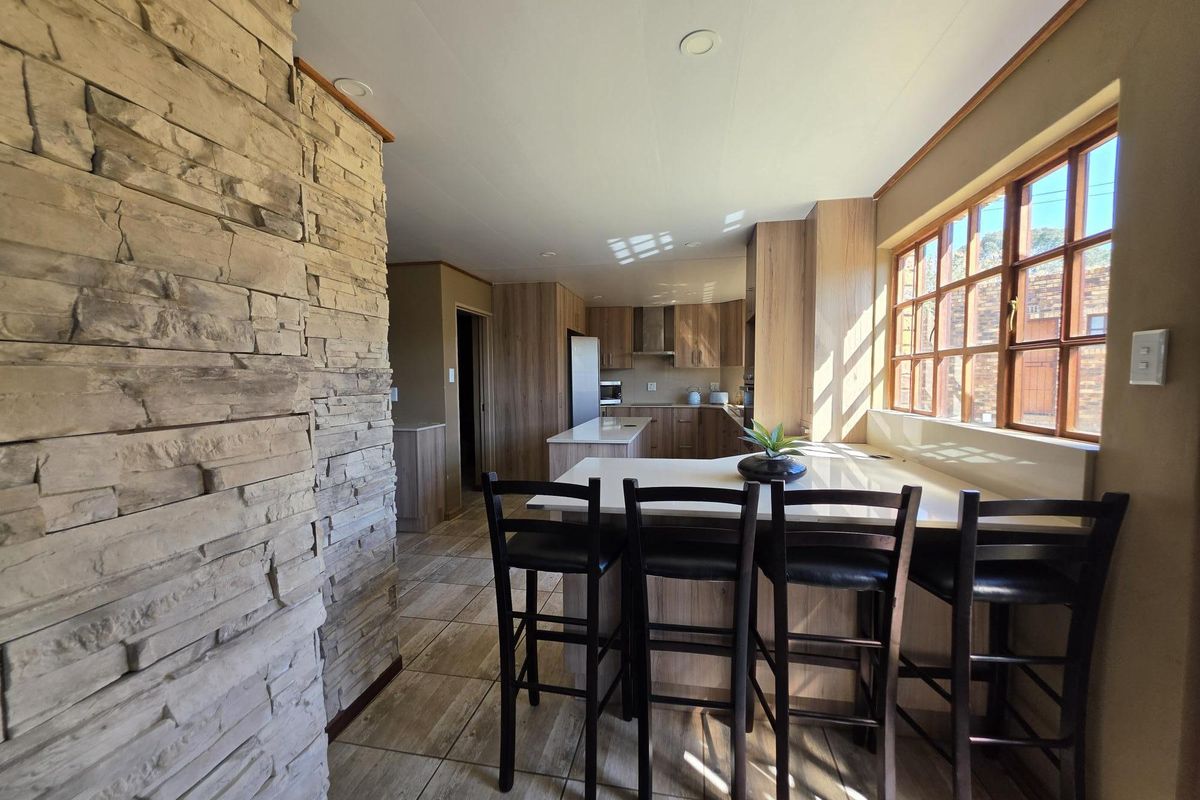 Modern kitchen featuring wood-look cabinetry, stone countertops, a central island with breakfast bar seating, and a striking stone feature wall.