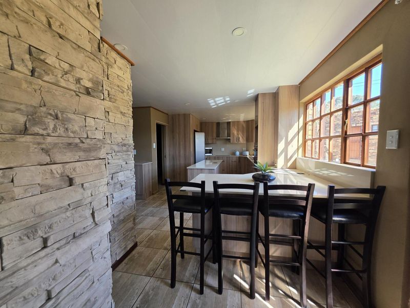 Modern kitchen featuring wood-look cabinetry, stone countertops, a central island with breakfast bar seating, and a striking stone feature wall.