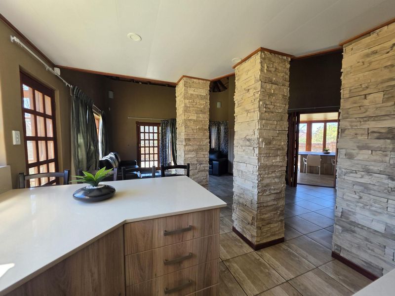 Open-plan living area featuring stone-clad columns, tiled flooring, and a modern kitchen island with stone countertops, connecting to an outdoor patio space.
