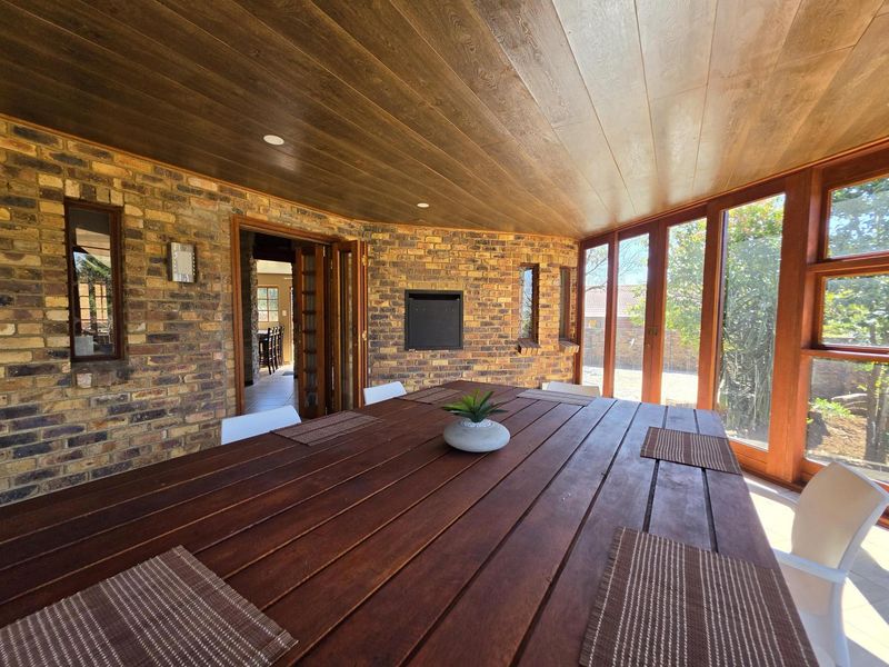 A covered patio featuring exposed brick walls, a timber-paneled ceiling, and large timber-framed windows, providing a warm and inviting outdoor entertainment space.