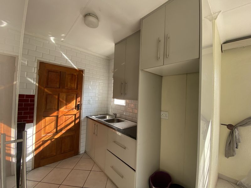 A compact scullery or utility area featuring modern grey cabinetry, a stainless steel sink, and subway tile backsplash with tiled flooring.