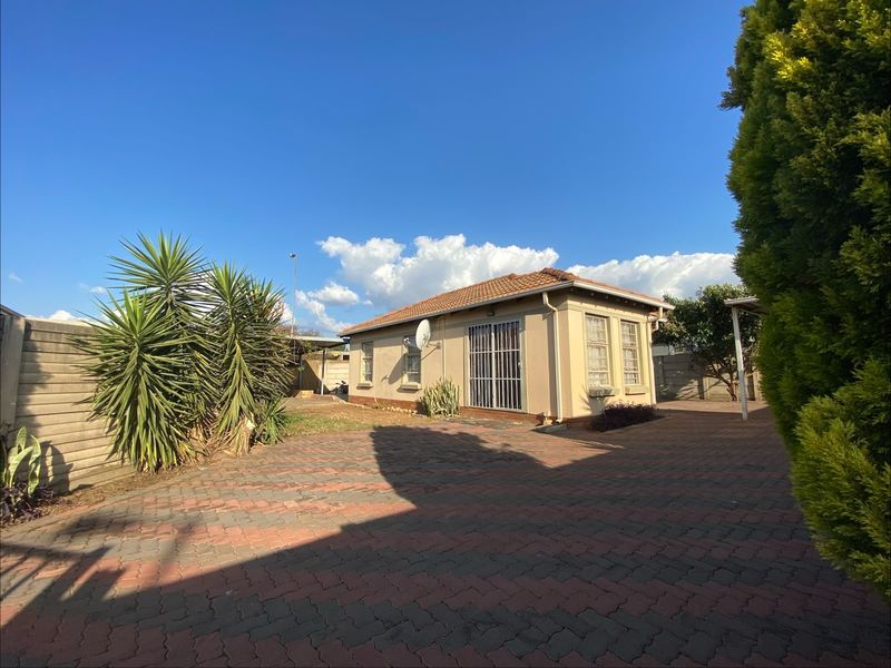 Rear view of the property featuring a paved driveway, terracotta tiled roof, and secure sliding door access to the home.