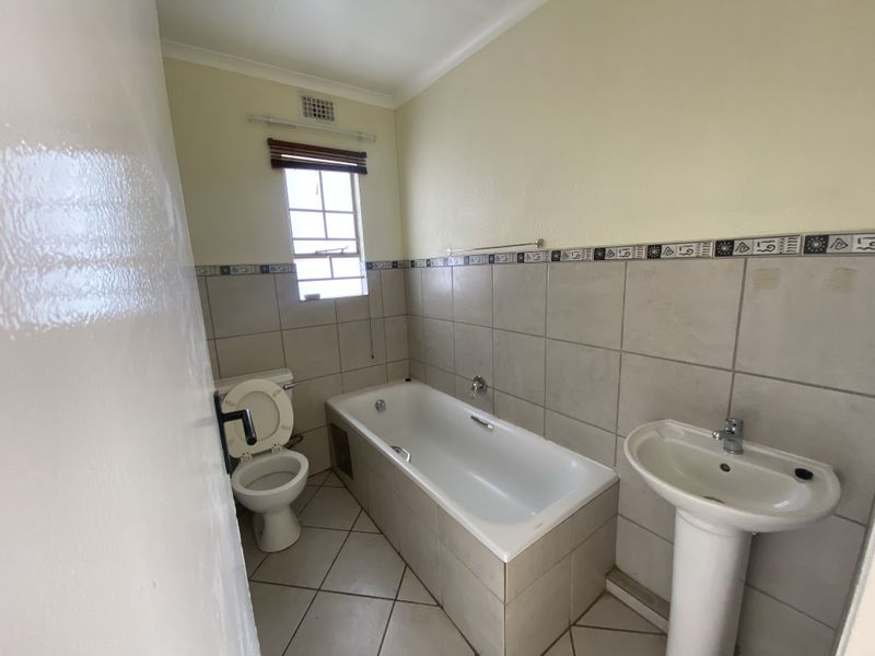 A functional bathroom featuring a bathtub, pedestal basin, and toilet with neutral wall and floor tiling.