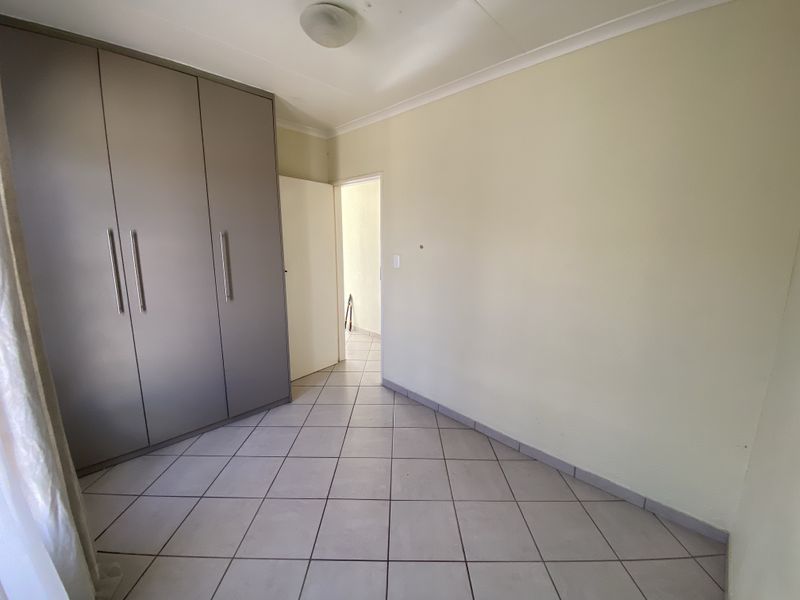 A clean, empty bedroom featuring neutral tiled flooring, built-in cupboards, and simple cove cornicing, offering a blank canvas for personalization.