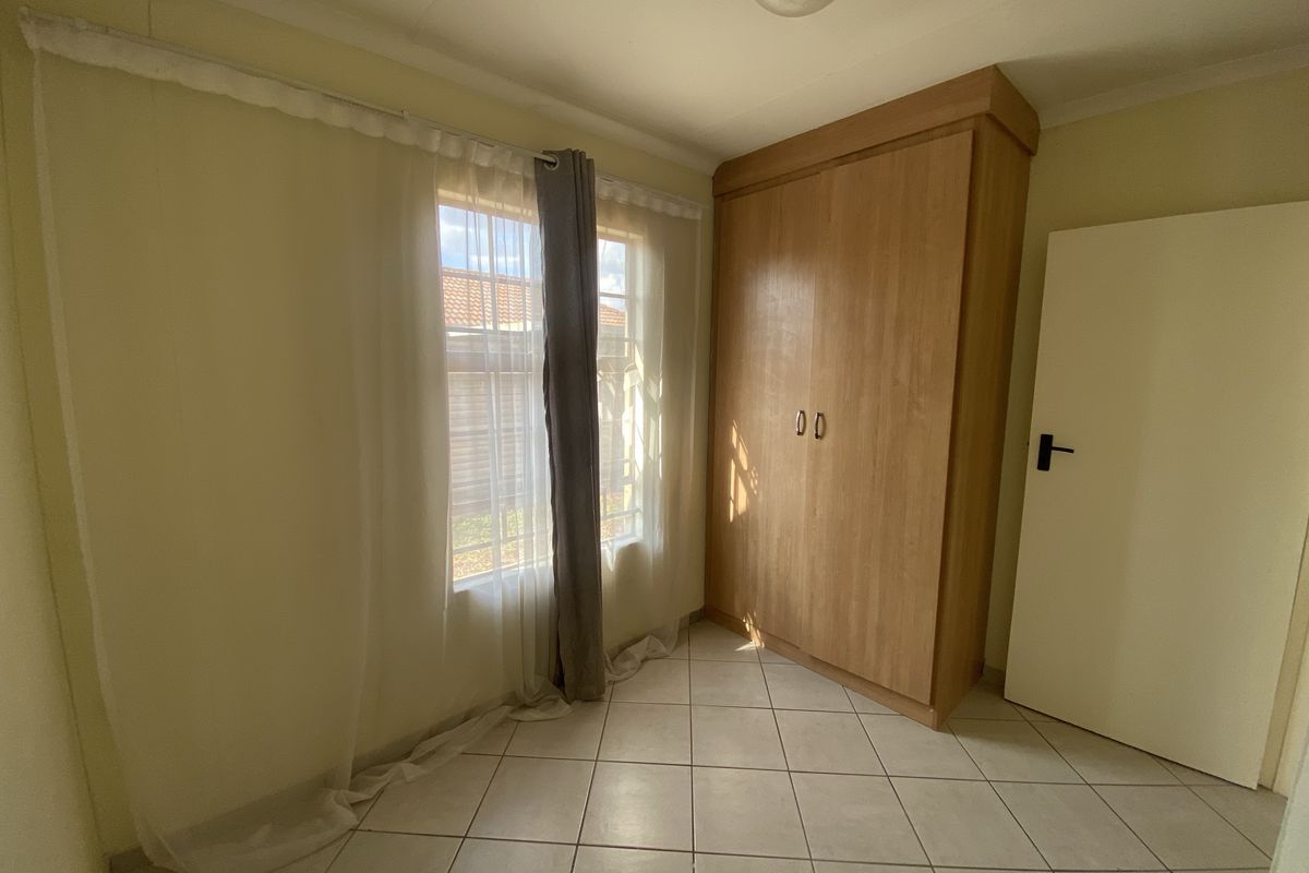 A bright, empty bedroom featuring tiled flooring and a built-in wooden wardrobe, offering a clean and neutral space ready for personalization.