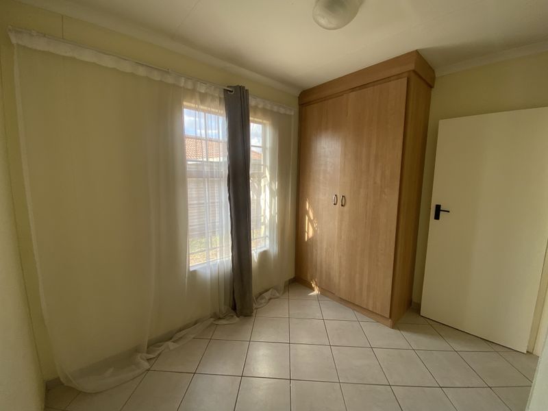 A bright, empty bedroom featuring tiled flooring and a built-in wooden wardrobe, offering a clean and neutral space ready for personalization.