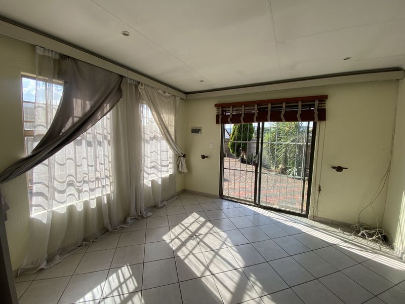 A bright, empty living room featuring tiled flooring, recessed lighting, and a sliding glass door providing access to the rear patio area.