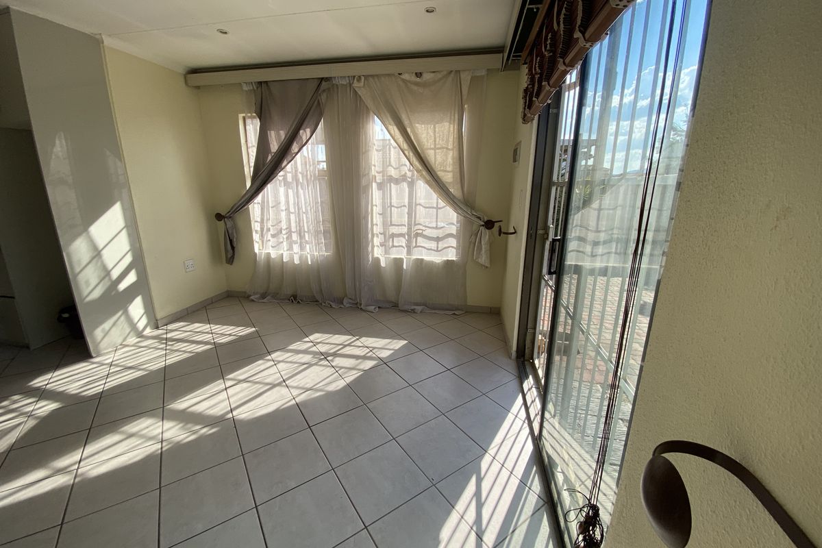 A bright, empty living area featuring neutral tiled flooring, recessed lighting, and large sliding glass doors providing access to the exterior.