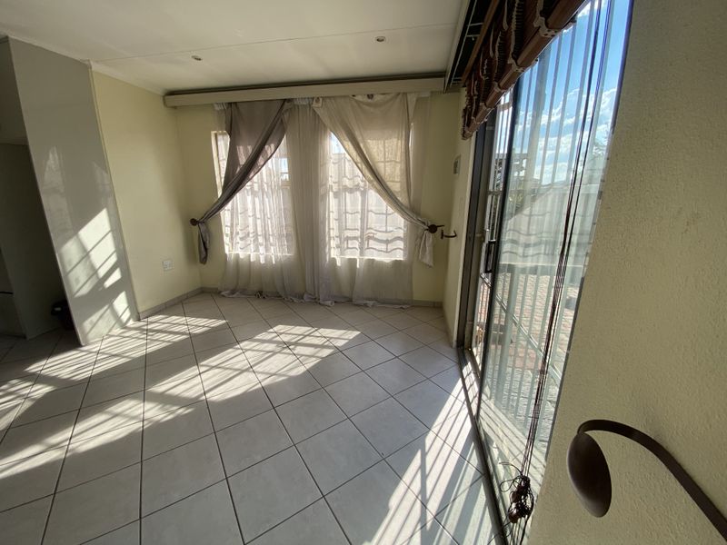 A bright, empty living area featuring neutral tiled flooring, recessed lighting, and large sliding glass doors providing access to the exterior.