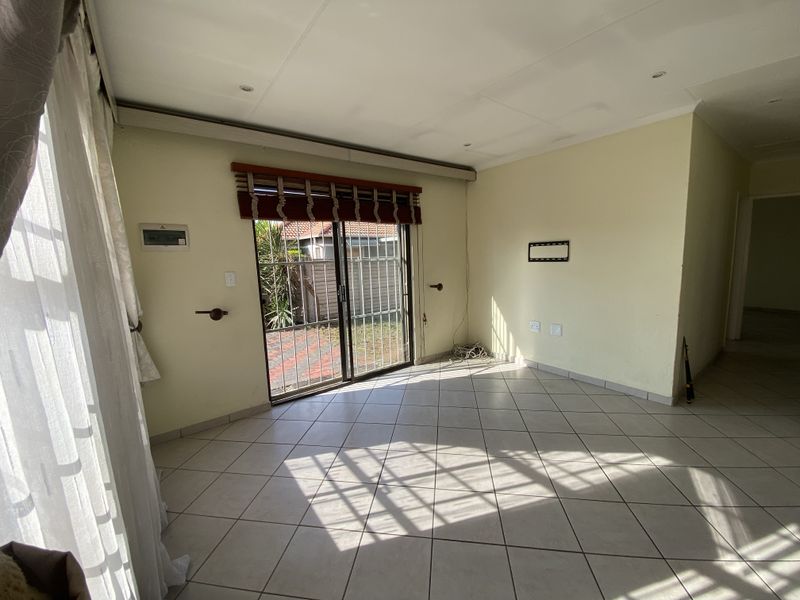 An empty living room featuring tiled flooring, recessed lighting, and a sliding glass door with a security gate leading to the exterior.