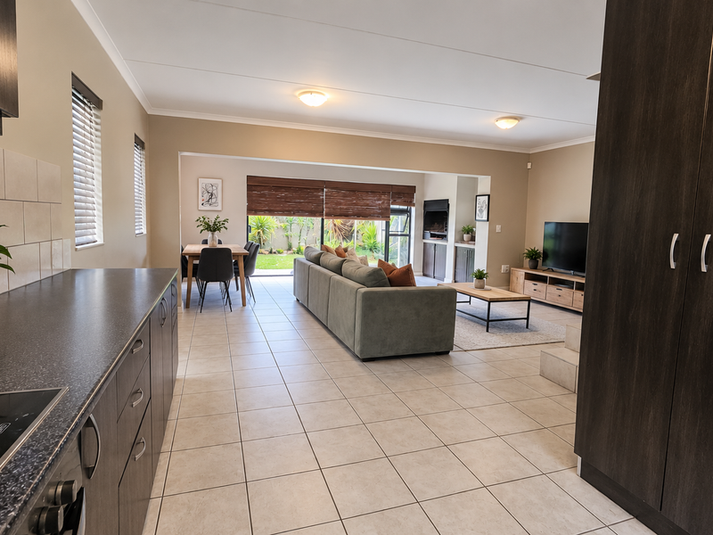 Spacious open-plan living area featuring a modern kitchen with dark cabinetry, tiled floors, and seamless flow to the outdoor patio through sliding glass doors.