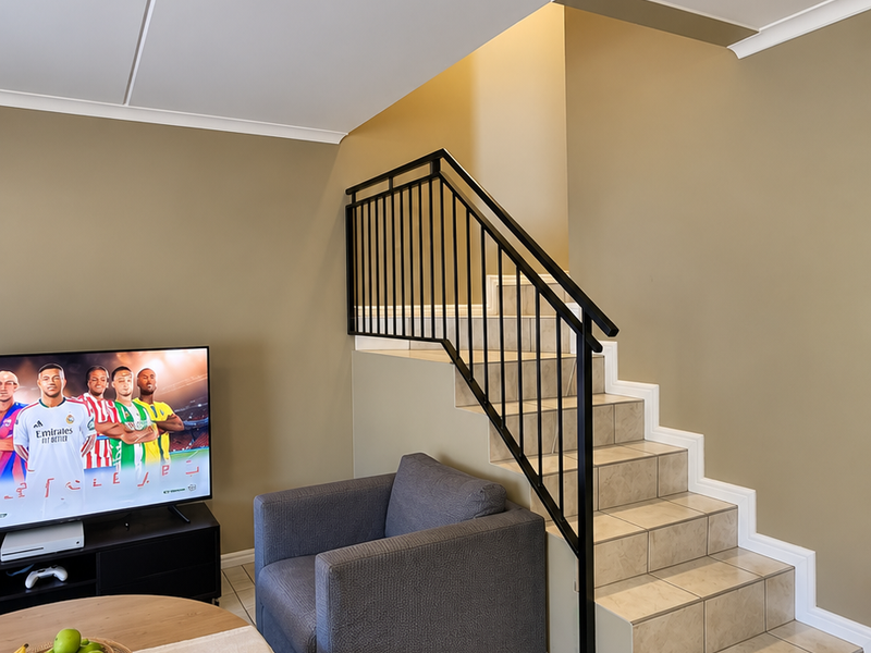 A living room area featuring a tiled staircase with a modern black metal balustrade and neutral wall tones.