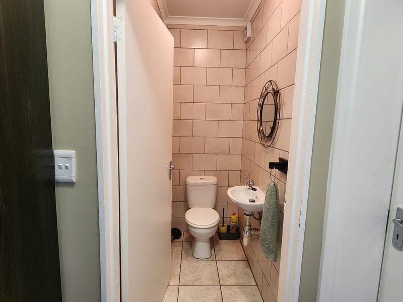 A compact guest bathroom featuring a toilet, wall-mounted basin, and neutral tiled finishes.