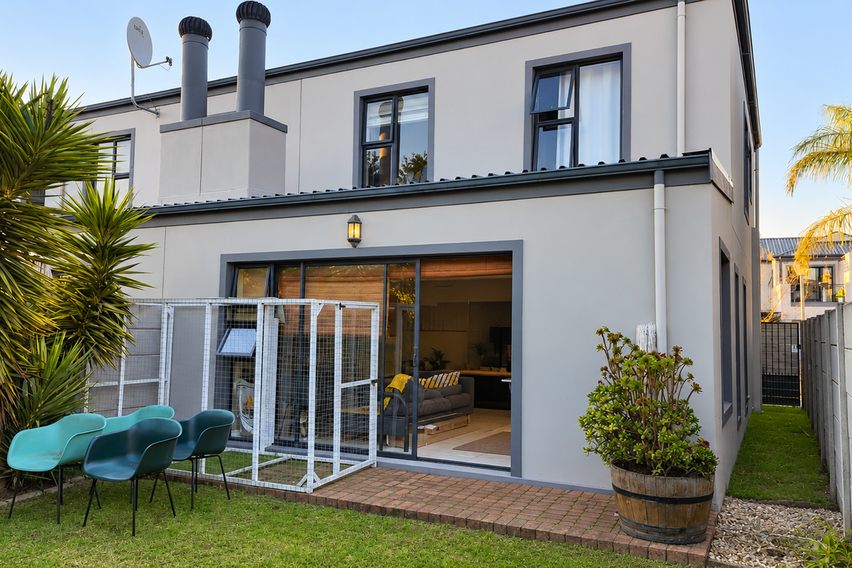 Rear view of a modern townhouse featuring a paved patio area, sliding glass doors, and a private garden with boundary walling.