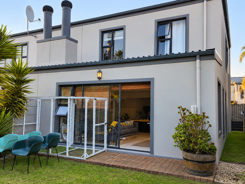 Rear view of a modern townhouse featuring a paved patio area, sliding glass doors, and a private garden with boundary walling.