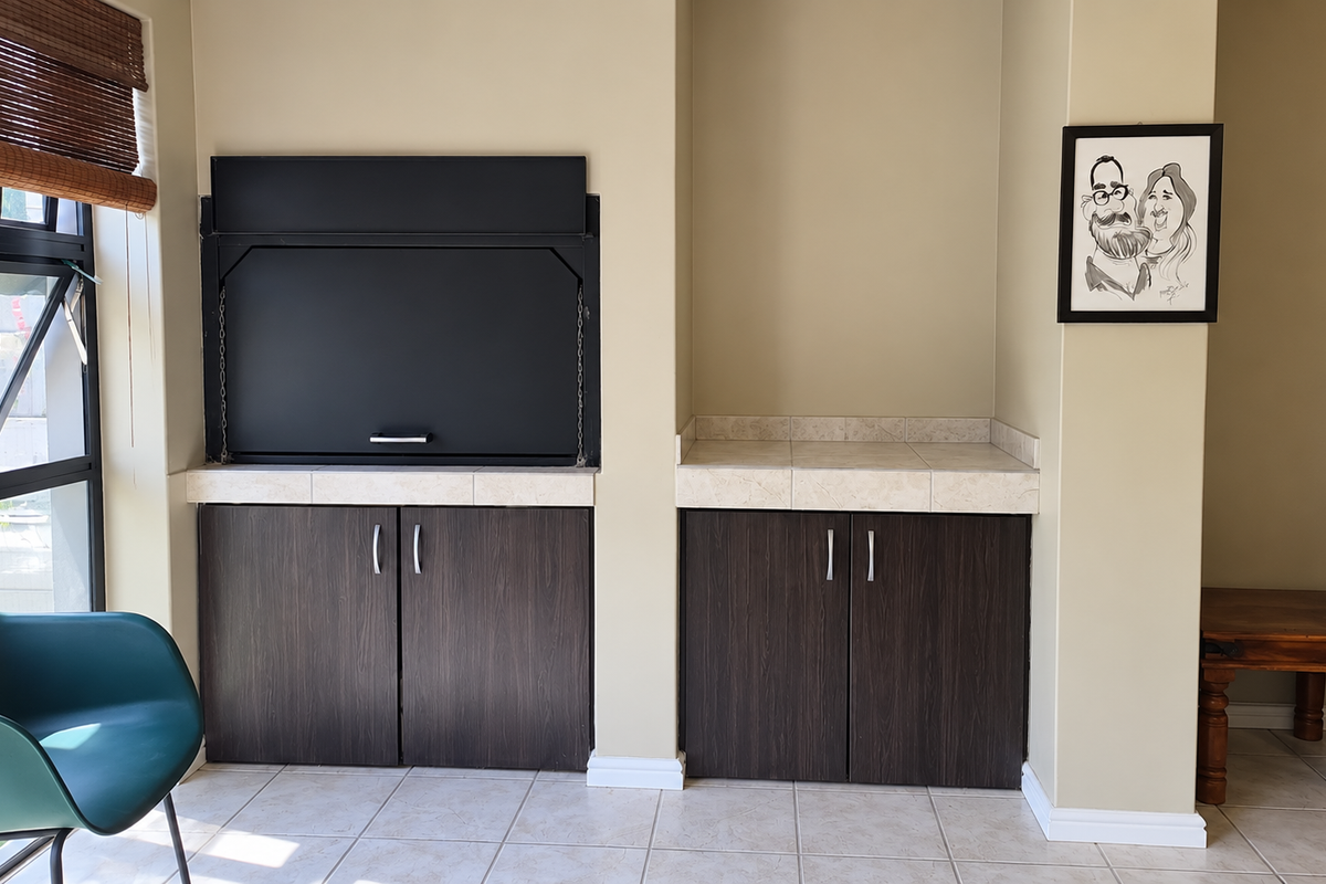 A living area featuring a built-in braai with dark cabinetry, tiled countertops, and neutral wall finishes, providing a functional indoor entertainment space.