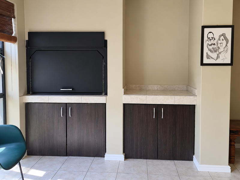 A living area featuring a built-in braai with dark cabinetry, tiled countertops, and neutral wall finishes, providing a functional indoor entertainment space.