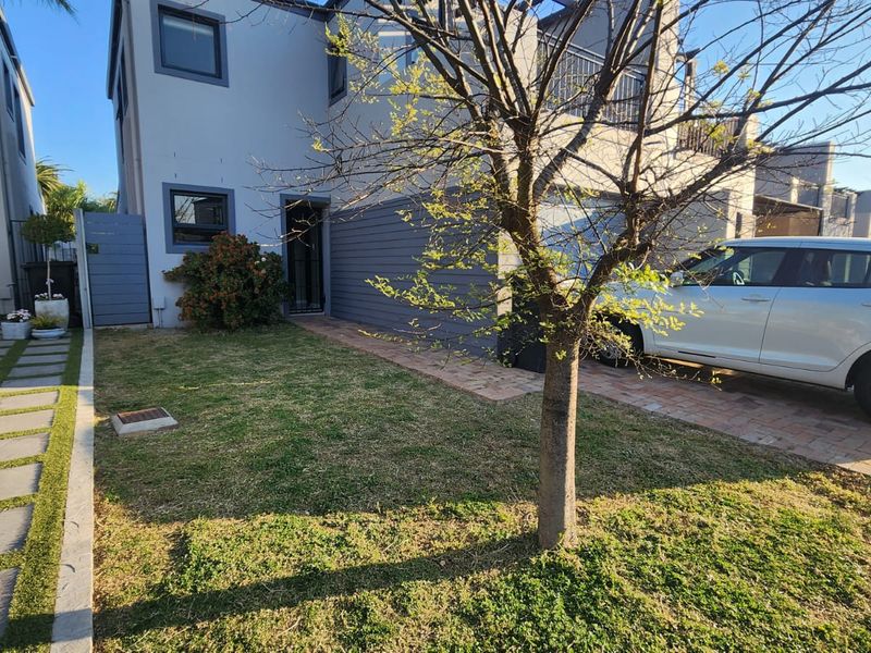 Front exterior view of a modern townhouse featuring a paved driveway, landscaped lawn, and a secure entrance with a balcony above.