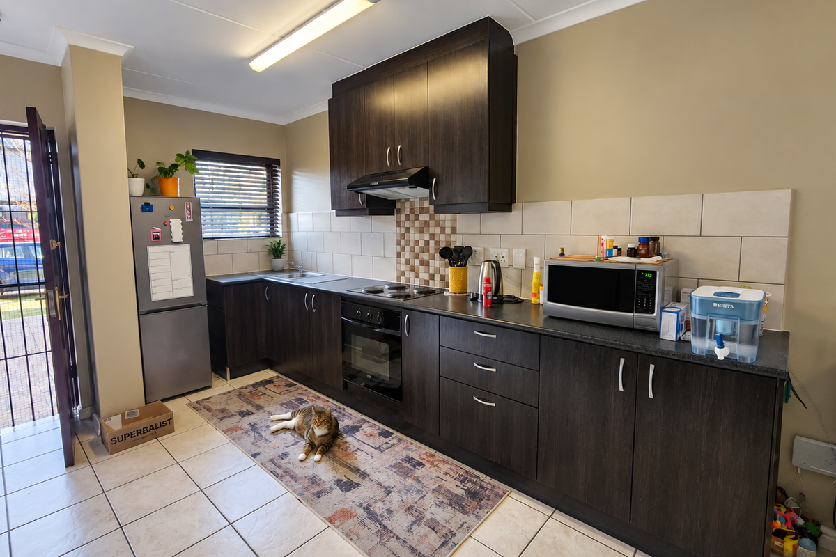 A functional kitchen featuring dark wood cabinetry, laminate countertops, built-in oven, electric hob, and tiled flooring with direct access to the exterior.
