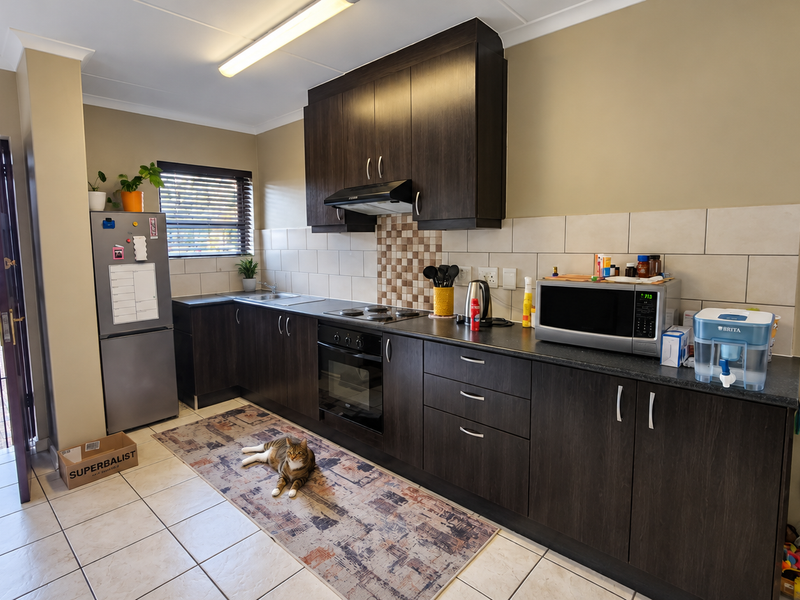 A functional kitchen featuring dark wood cabinetry, laminate countertops, built-in oven, electric hob, and tiled flooring with direct access to the exterior.