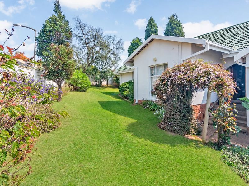 A well-maintained rear garden featuring a lush lawn, established landscaping, and a paved pathway leading to the side entrance of the house.