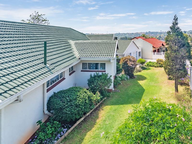 An elevated view of the rear exterior of the house, featuring a tiled roof, well-maintained garden, and boundary wall.