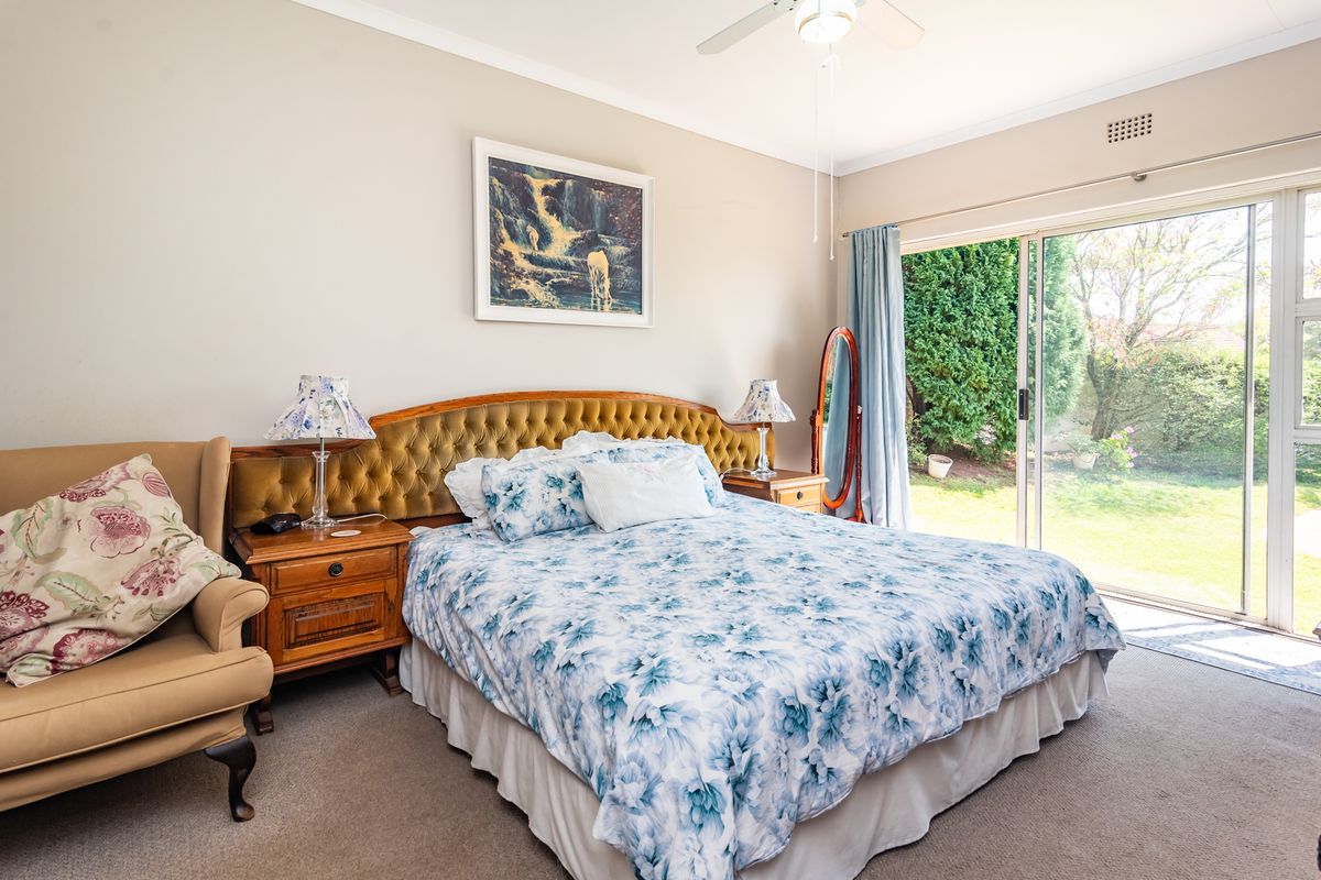 A well-lit bedroom featuring carpet flooring, a ceiling fan, and large sliding glass doors providing direct access to the garden.