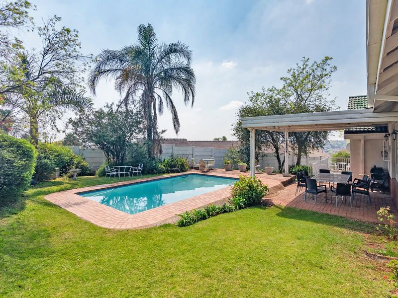A well-maintained outdoor area featuring a swimming pool with brick coping, a covered patio space, and a landscaped garden with mature trees.