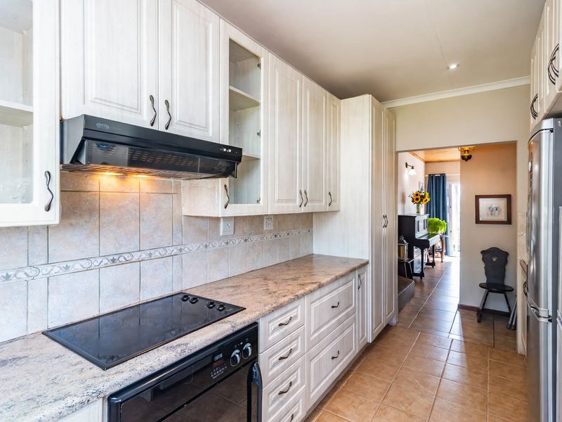A functional kitchen featuring white cabinetry, laminate countertops, a tiled backsplash, and integrated cooking appliances, with tiled flooring throughout.