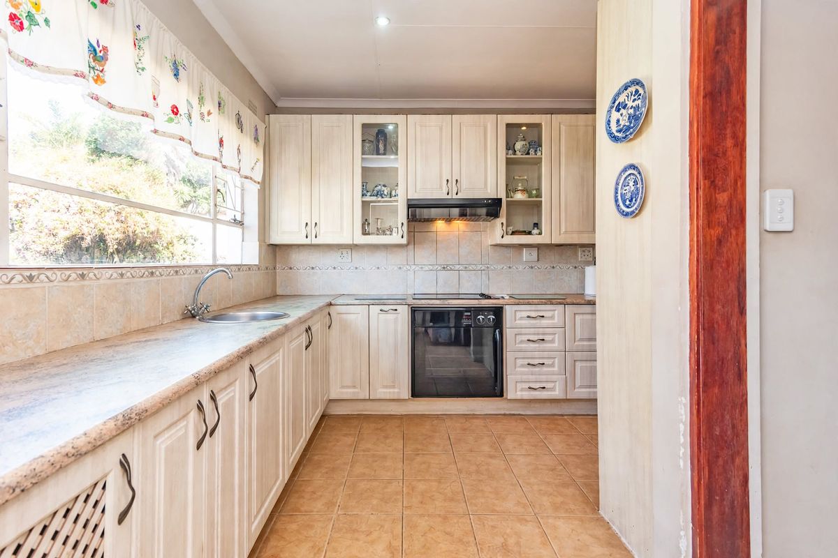 A functional kitchen featuring light-toned cabinetry, tiled backsplash, built-in oven with extractor fan, and ample counter space with a stainless steel sink.