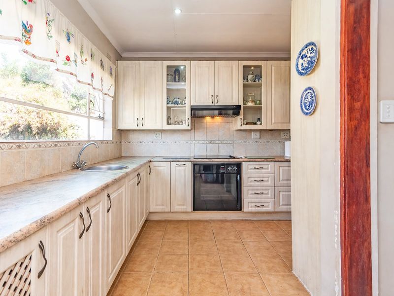 A functional kitchen featuring light-toned cabinetry, tiled backsplash, built-in oven with extractor fan, and ample counter space with a stainless steel sink.