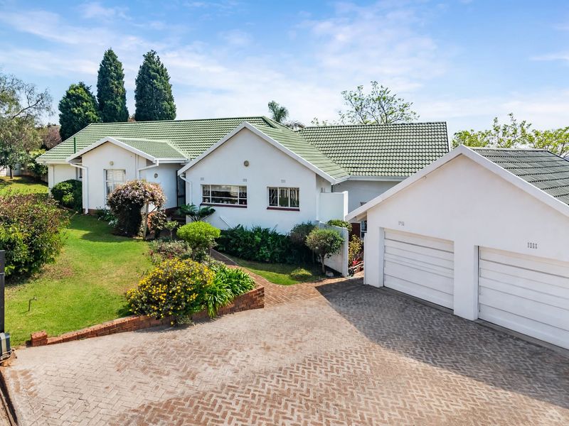Front view of a well-maintained single-story house featuring a green tiled roof, double garage, paved driveway, and established garden.