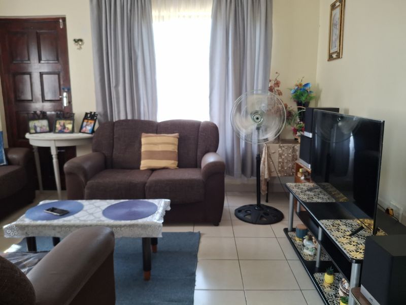 A functional living room featuring tiled flooring and large windows with curtain tracks, providing a comfortable and well-lit space.