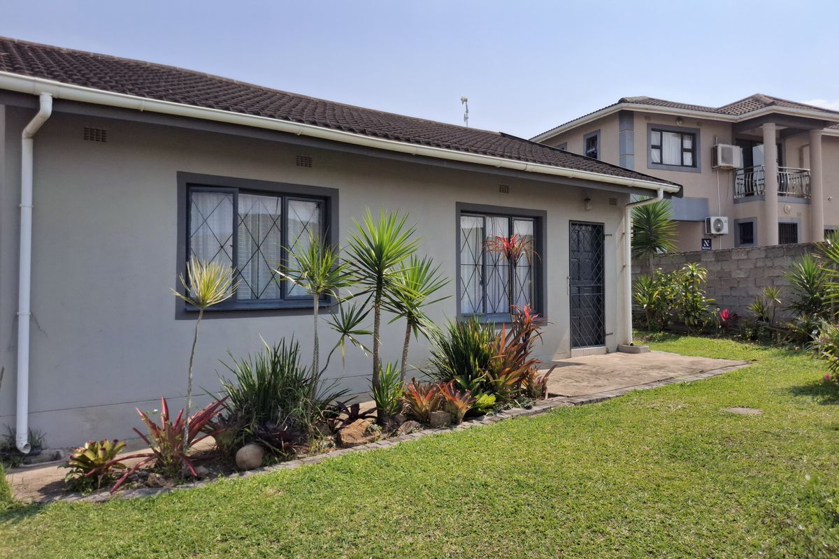 Rear view of the house featuring a concrete patio, landscaped garden, and secure window and door fixtures.