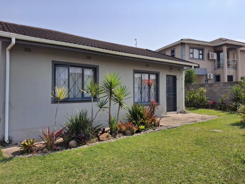 Rear view of the house featuring a concrete patio, landscaped garden, and secure window and door fixtures.
