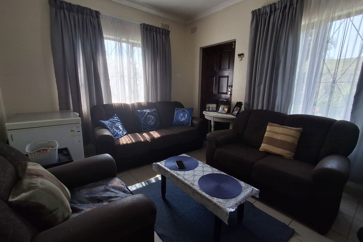 A functional living room featuring tiled flooring, natural light through large windows with security gates, and direct access to the home entrance.