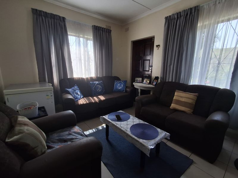 A functional living room featuring tiled flooring, natural light through large windows with security gates, and direct access to the home entrance.