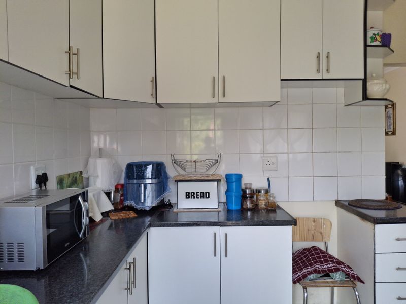 A functional kitchen featuring white laminate cabinetry, dark granite countertops, and white ceramic wall tiling.