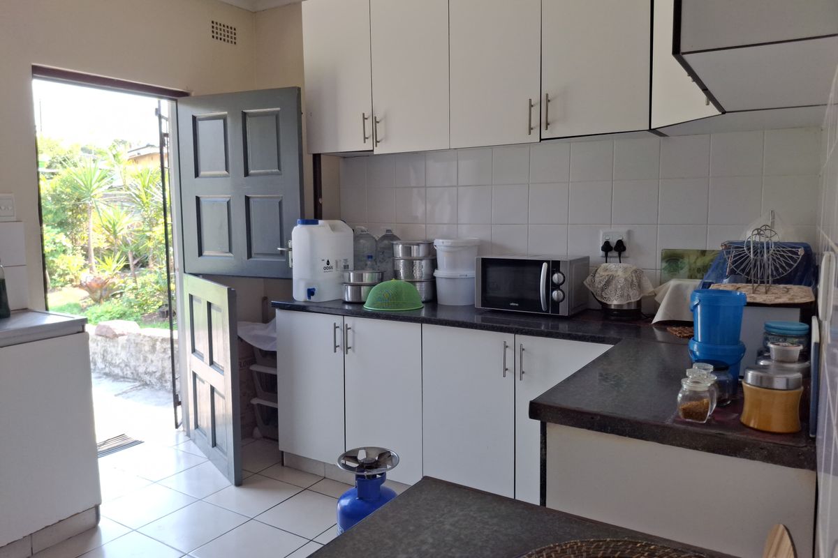 A functional kitchen featuring white cabinetry, dark laminate countertops, tiled backsplash, and direct access to the garden via a stable door.