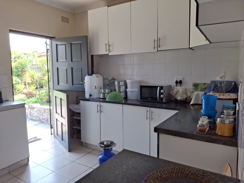 A functional kitchen featuring white cabinetry, dark laminate countertops, tiled backsplash, and direct access to the garden via a stable door.