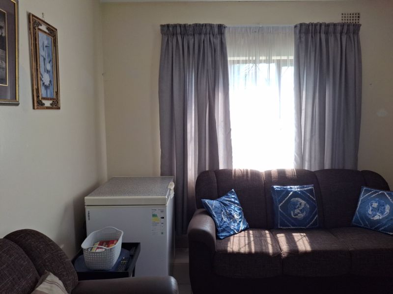 A living room area featuring a window with curtains and a wall-mounted air vent.