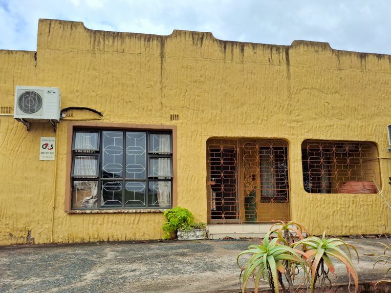 Front elevation of a house featuring a textured yellow facade, security gates, and multiple air conditioning units installed on the exterior walls.