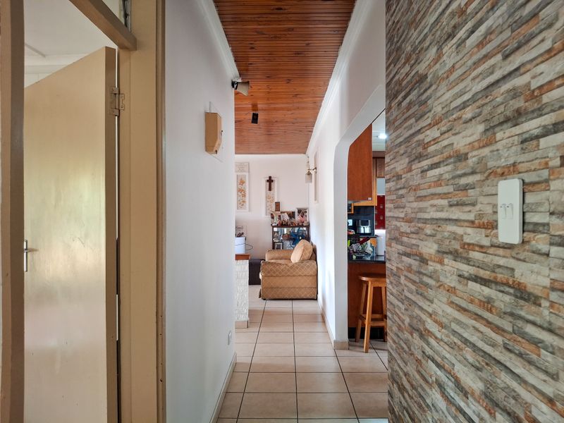 A hallway featuring a timber slat ceiling, ceramic floor tiles, and a decorative stone-clad feature wall, leading towards the living and kitchen areas.
