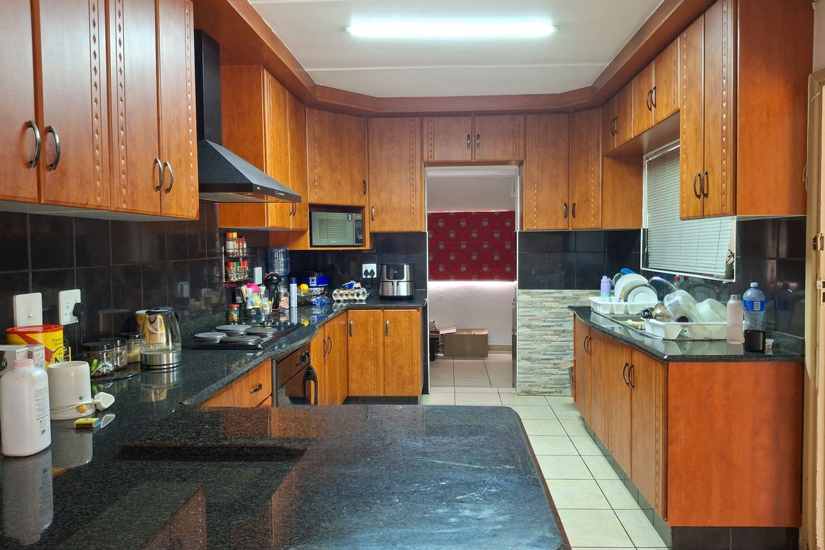 A functional kitchen featuring extensive wooden cabinetry, granite countertops, a built-in oven, hob, and extractor fan with a tiled backsplash.